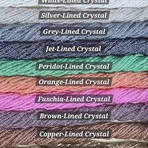May include: Ten horizontal rows of twisted cord trim, each featuring a distinct color with a crystal-lined finish. The rows are labeled White-Lined Crystal, Silver-Lined Crystal, Grey-Lined Crystal, Jet-Lined Crystal, Peridot-Lined Crystal, Orange-Lined Crystal, Fuschia-Lined Crystal, Brown-Lined Crystal, Copper-Lined Crystal, and Gold-Lined Crystal.