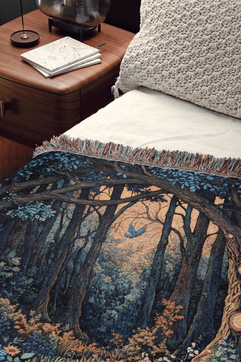 May include: A woven throw blanket featuring a detailed forest scene with dark blue and brown trees, a small blue bird in flight, and a light-colored sky. The blanket has a textured surface and a decorative fringe along the top edge with multi-colored threads.