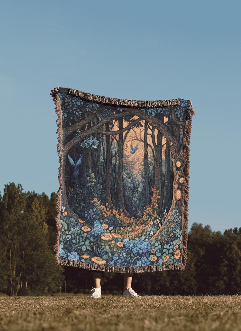 May include: A rectangular woven throw blanket featuring a detailed forest scene with dark blue and brown trees, orange and blue flowers, and two blue birds. The blanket has a fringed edge on the top and bottom and a circular frame design.