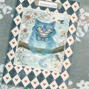 May include: A vintage-style card featuring a blue Cheshire Cat illustration and the word "WONDERLAND" in a banner. The card has a chequered background with red hearts.