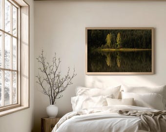 Può includere: Una fotografia incorniciata di un paesaggio raffigura una serena scena lacustre con lussureggianti alberi verdi e il loro riflesso nell'acqua. L'opera d'arte è esposta sopra un letto con biancheria da letto bianca, creando un'estetica rilassante della camera da letto.