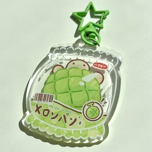 May include: A clear acrylic keychain featuring a green melon bread design inside a jar. The keychain has a green star-shaped clasp. Japanese text and a barcode are visible on the design.