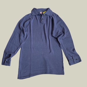 Könnte beinhalten: Ein marineblaues Langarmhemd mit Kragen und Knopfverschluss. Das Hemd hat geknöpfte Manschetten und eine lockere Passform. Ein gelbes Etikett ist am Kragen befestigt.