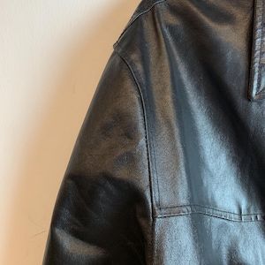 May include: Close-up of a black leather jacket, showcasing the shoulder and collar details. The jacket has visible stitching and a textured surface, suggesting a high-quality garment. The leather appears to be supple and well-maintained.