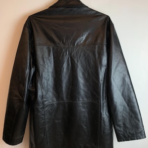 May include: A black leather jacket with a collared neckline and long sleeves. The jacket is hanging on a metal hanger against a white background. The back of the jacket is visible, showing the seams and stitching details.