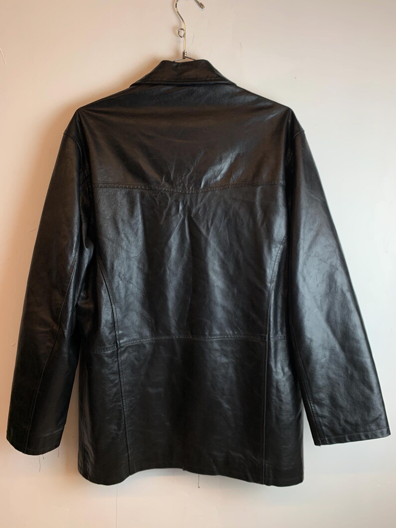 May include: A black leather jacket with a collared neckline and long sleeves. The jacket is hanging on a metal hanger against a white background. The back of the jacket is visible, showing the seams and stitching details.