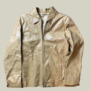 Può includere: Giacca in pelle color cuoio con chiusura a zip integrale. La giacca presenta un collo, maniche lunghe con polsini abbottonati e una vestibilità su misura. La pelle ha un aspetto leggermente usurato.