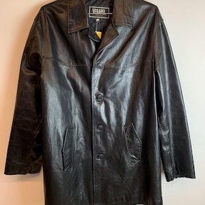 May include: Black leather coat with a button-up front, two front pockets, and a collared neckline. The coat is hanging on a metal hanger. The label reads "VERAPEL".
