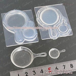 May include: Clear silicone mold for making miniature frying pans and a hand mirror. The mold is on a gray surface with a ruler marked in inches.
