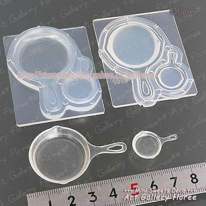 May include: Clear silicone mold for making miniature frying pans and a hand mirror. The mold is on a gray surface with a ruler marked in inches.