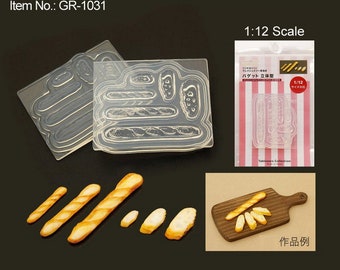 May include: A clear plastic mold for making miniature baguettes, with a sample of the finished product on a wooden cutting board. The mold is labeled "Baguette 3D Mold" and "1/12 Size".