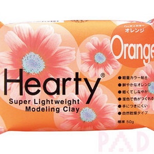 Peut inclure: Pâte à modeler orange Hearty Super Lightweight, un paquet de 50g d'argile orange avec un motif floral. L'emballage présente du texte japonais décrivant les propriétés de l'argile.