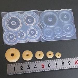 May include: A silicone mold with six different sized donut shapes. The mold is clear and has a textured surface. There are five donuts made with resin in the sizes shown on a ruler.