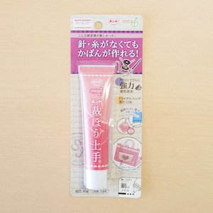 Puede incluir: Un tubo rosa de pegamento para tela con el texto "ポンド 裁ほう上手" en japonés. El empaque muestra una bolsa con un bolsillo en forma de corazón y el texto "針・糸がなくても かばんが作れる!" en japonés, que se traduce como "¡Puedes hacer una bolsa sin agujas ni hilo!"