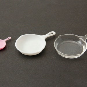 May include: Three miniature frying pans in different sizes and colors: pink, white, and clear.