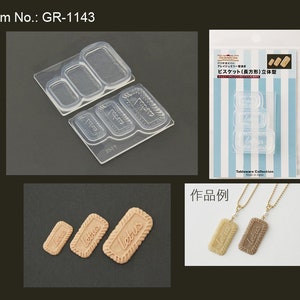 Könnte beinhalten: Eine transparente Plastikform zum Herstellen von rechteckigen Keksen. Die Form hat drei verschiedene Größen von rechteckigen Formen. Die Form wird neben einer Probe der Kekse gezeigt, die mit der Form hergestellt werden können. Die Kekse sind braun und haben den Schriftzug "Letus" aufgedruckt.