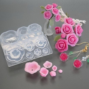 Puede incluir: Un conjunto de rosas de arcilla polimérica rosa, un molde de silicona transparente con formas de rosas y un par de pendientes con rosas de arcilla polimérica rosa. Las rosas son de varios tamaños y formas.