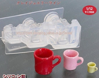 May include: A clear silicone mold for making miniature mugs. The mold has three cavities, each shaped like a mug. The mold is labeled "Cray Jewelry Line" and "1/12 Size Compatible".