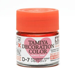 Peut inclure: Petite bouteille en verre de peinture acrylique Tamiya Decoration Color, étiquetée D-7 Strawberry Syrup. Le flacon a un bouchon orange vif et contient un liquide rouge. L'étiquette comporte du texte en anglais et en japonais.