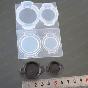 Może przedstawiać: Dwa przezroczyste silikonowe formy do tworzenia okrągłych przedmiotów z żywicy. Formy są pokazane obok dwóch gotowych przedmiotów z żywicy, jednego dużego i jednego małego, z linijką do skalowania.