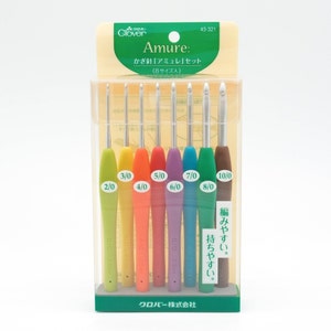 Può includere: Un set di otto uncinetti colorati in una confezione di plastica trasparente. Gli uncinetti sono etichettati con le dimensioni 2/0, 3/0, 4/0, 5/0, 6/0, 7/0, 8/0 e 10/0. La confezione è etichettata con "Amure: かぎ針 "アミュレ" セット (8サイズ入)" e "クロバー株式会社".