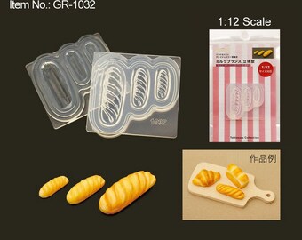 May include: A clear plastic mold for making miniature French bread loaves. The mold has three cavities, each shaped like a loaf of bread. The mold is labeled "Milk French Bread 3D Mold" and "1/12 Size".