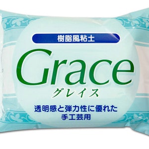 Op de afbeelding: Een witte plastic zak met een blauw en groen label. Het label zegt "Harsklei" in het Japans en "Grace" in het Engels. Het label zegt ook "Transparant en elastisch, ideaal voor ambachten".