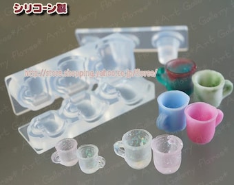 Peut inclure: Un moule en silicone pour faire des tasses à thé miniatures. Le moule est transparent et comporte six cavités, chacune en forme de tasse à thé différente. Il y a aussi plusieurs tasses à thé miniatures faites avec le moule, dans différentes couleurs, dont le rose, le bleu, le vert et le transparent.