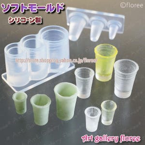 May include: Clear silicone molds for crafting, featuring various cup shapes and sizes. The image includes molds with three connected cups, individual cups, and finished resin cups in green and yellow. Text in Japanese reads "Soft Mold" and "Silicone Made."
