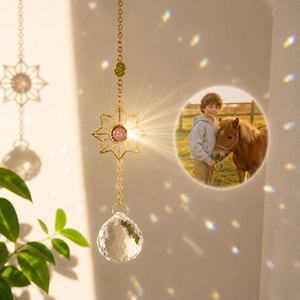 May include: A gold-toned suncatcher featuring a star-shaped metal frame with a central pink stone, a hanging clear crystal sphere, and a circular photo insert showing a child standing next to a brown horse, suspended by a delicate metal chain.