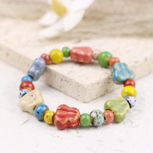 May include: A vibrant ceramic bead bracelet. The beads are in various shapes and sizes, with colours including red, yellow, blue, green, and cream. The bracelet is strung on an elastic cord, and the beads are measured in centimetres.