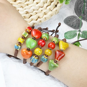 May include: Colorful ceramic beaded bracelets. Each bracelet features a variety of shapes and colors, including red, green, yellow, and blue beads. The beads are strung on brown cords, creating a unique and artistic accessory.