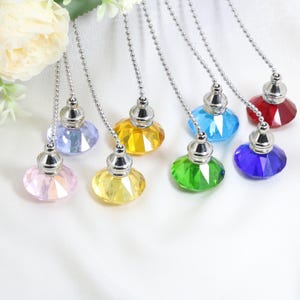Puede incluir: Ocho cadenas de tracción de cristal en varios colores, incluyendo rosa, amarillo, azul, verde y rojo. Cada cadena tiene una parte superior de metal plateado y una parte inferior de cristal facetado.