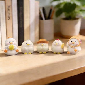 May include: A row of five small, white chick figurines with various accessories. One holds a yellow object, another has a straw hat, and a third has a pink flower. The figurines have black dot eyes and orange feet.