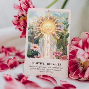 May include: An oracle card with the text "POSITIVE THOUGHTS" and an illustration of a sun with a face, surrounded by flowers and greenery. Pink and red flower petals are scattered around the card.