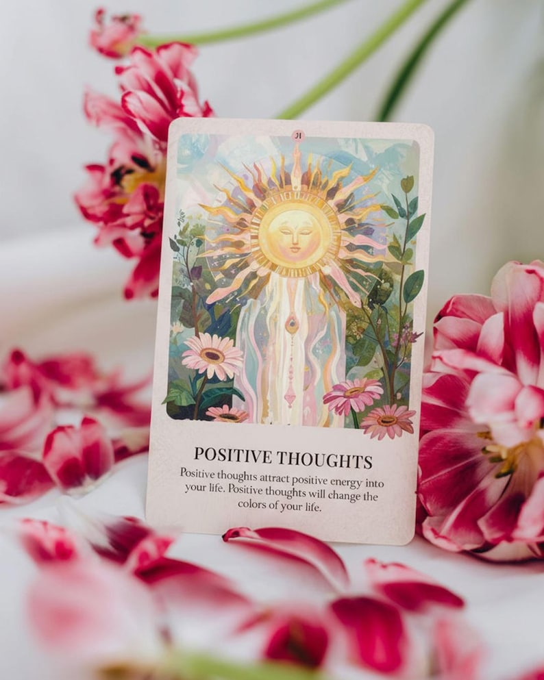 May include: An oracle card with the text "POSITIVE THOUGHTS" and an illustration of a sun with a face, surrounded by flowers and greenery. Pink and red flower petals are scattered around the card.