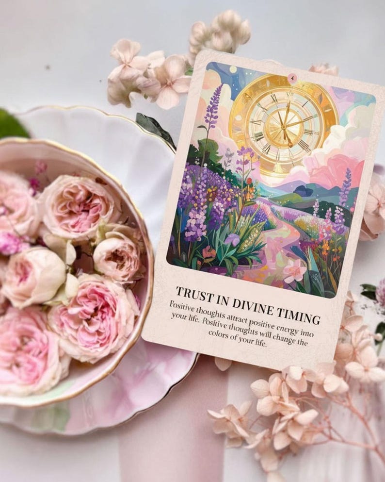 May include: An oracle card with the text "TRUST IN DIVINE TIMING" and a colorful illustration of a clock, flowers, and a path. Pink roses in a decorative dish and delicate flowers surround the card, creating a soft, feminine aesthetic.