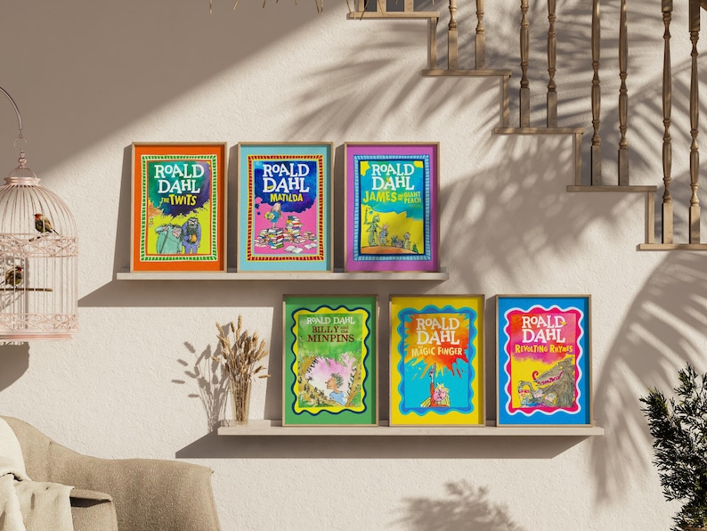 May include: A display of framed Roald Dahl book covers, such as "The Twits" and "Matilda." The colourful illustrations are presented on shelves against a neutral wall. The image includes a decorative birdcage and a staircase in the background, creating a warm atmosphere.