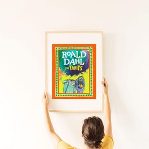 May include: A framed print of the book cover for Roald Dahl's "The Twits." The artwork features a vibrant orange border, a green and blue central design, and illustrations of the characters. The title is prominently displayed in white and green.