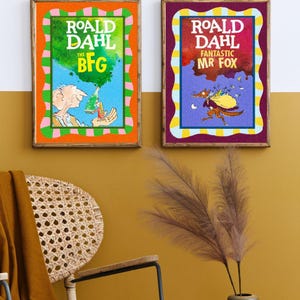 May include: Two framed book covers of Roald Dahl's "The BFG" and "Fantastic Mr. Fox." The BFG cover has an orange border and a green and blue background. The Mr. Fox cover has a purple border and a red and blue background. Both are in wooden frames.