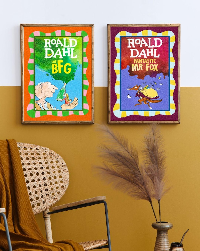 May include: Two framed book covers of Roald Dahl's "The BFG" and "Fantastic Mr. Fox." The BFG cover has an orange border and a green and blue background. The Mr. Fox cover has a purple border and a red and blue background. Both are in wooden frames.