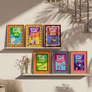 May include: A collection of six framed Roald Dahl book covers adorns a wall. The vibrant illustrations and titles, including "BFG" and "Charlie and the Chocolate Factory," are displayed in colorful frames. The arrangement creates a visually appealing display.