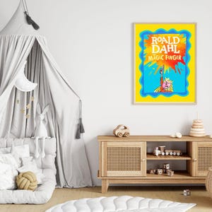 May include: A framed print of "Roald Dahl The Magic Finger" with a yellow border and blue accents. The artwork features a colorful illustration of a character pointing upwards, set against a blue and orange background. The print is displayed in a child's room.