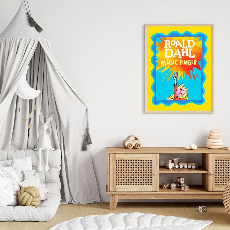 May include: A framed print of "Roald Dahl The Magic Finger" with a yellow border and blue accents. The artwork features a colorful illustration of a character pointing upwards, set against a blue and orange background. The print is displayed in a child's room.