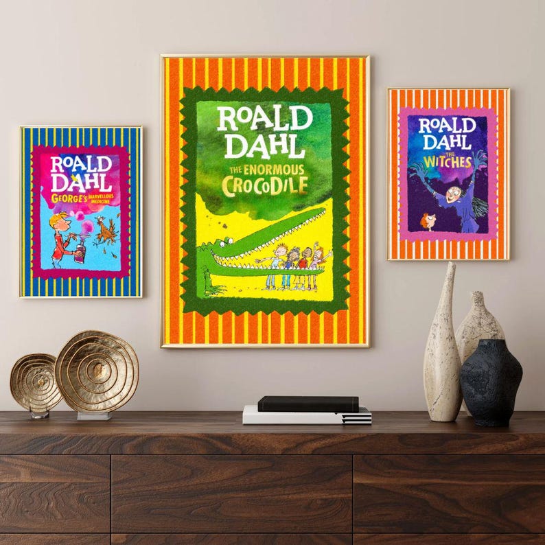 May include: Three framed book covers by Roald Dahl are displayed. The titles are "George's Marvellous Medicine", "The Enormous Crocodile", and "The Witches". Each cover has colourful illustrations and text, with a striped border. The frames are gold.
