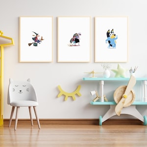 May include: Three framed illustrations on a white wall. The illustrations are of a witch flying on a broomstick, a monster with a red cape, and a blue dog. The wall is decorated with a yellow eye shape and a white chair with a cat face.