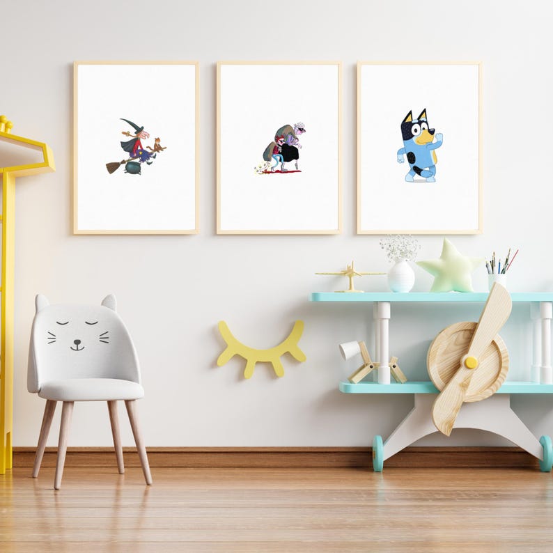 May include: Three framed illustrations on a white wall. The illustrations are of a witch flying on a broomstick, a monster with a red cape, and a blue dog. The wall is decorated with a yellow eye shape and a white chair with a cat face.