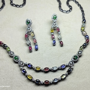 May include: A necklace and earring set with a silver-toned finish. The necklace and earrings feature a variety of colourful, oval-shaped gemstones. The necklace has two strands of gemstones. The earrings are dangling with a similar design.