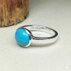 May include: A silver ring featuring a smooth, oval-shaped, bright turquoise stone set in a polished metal band. The interior of the band is clearly engraved with the text 925 Silver, indicating the metal composition of this jewelry piece.
