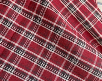 May include: A piece of fabric featuring a classic plaid pattern in shades of deep red, black, and white. The textile displays a woven texture with intersecting horizontal and vertical lines forming a repeating grid design across the entire surface.